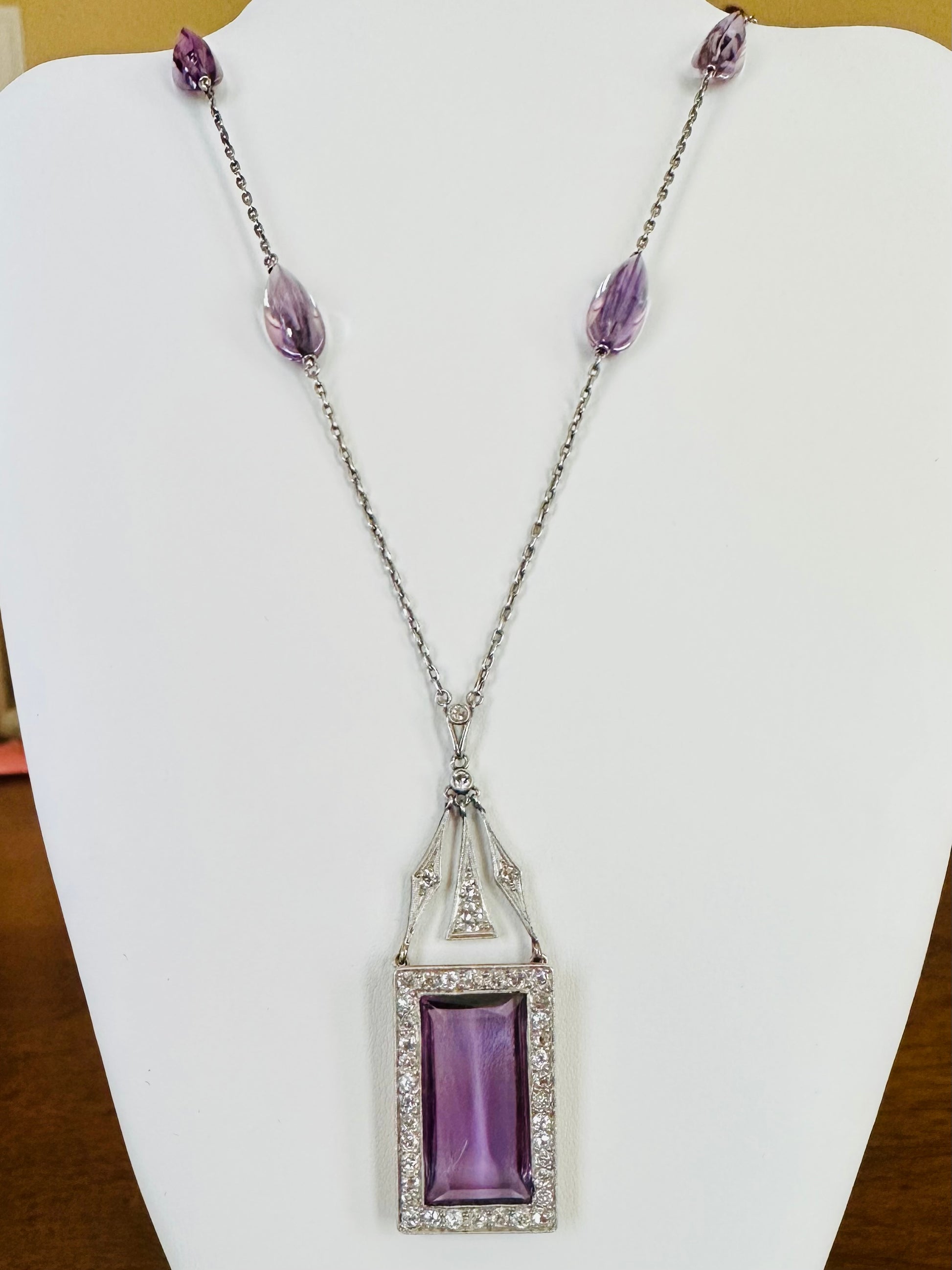 Art Deco rectangular purple amethyst pendant necklace framed by diamonds on white display stand 
